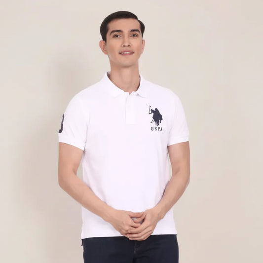 Man wearing a white polo shirt with a logo on a plain background